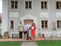 Eine fünfköpfige Familie vor einem sanierten Haus mit neuen Holz-Fenstern und türkisen Anstrich