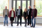 Beim Informationsbesuch der Bündnis 90/Die Grünen versammeln sich sechs Personen, davon zwei Damen und vier Herren für ein Gruppenfoto im Versammlungsraum des Verbandes für Ländliche Entwicklung Niederbayern. Durch die Glasfront im Hintergrund sind die Laubbäume am Isardamm zu sehen.