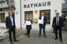 Drei Männer und eine Frau stehen vor dem Rathaus-Gebäude in Drachselsried. Bürgermeister Johannes Vogl und Kämmerin Julia Huber halten die Einleitungsurkunde der Dorferneuerung in den Händen.