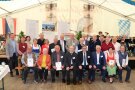 Gruppenfoto zum feierlichen Abschluss. 23 Personen posieren im Festzelt zum Abschluss-Foto des Projektes Niederwinkling-Welchenberg. Im Hintergrund sind einige Plakate über das Projekt der Ländlichen Entwicklung sowie mehrere Musikanten einer Blasmusikkapelle zu sehen.