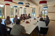 Mehrere Personen sitzen an einem Tisch und lauschen der Rede eines Mannes am Rednerpult