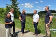 Vier Herren und eine Frau stehen auf einer asphaltierten Straße vor einer Wiese