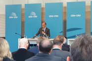 Mehrere sitzende Personen lauschen den Ausführungen des CDU/CSU-Parteivorsitzenden Friedrich Merz am Rednerpult