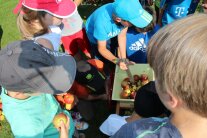 Mehrere Kinder stehen um eine Apfelpresse herum. Der Junge in der Bildmitte presst mit Hilfe eines Holzstabes die Äpfel klein. Die Kinder ringsherum halten Äpfel in ihren Händen.