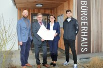 Drei Herren und eine Frau stehen vorm Haupteingang zum neuen Bürgerhaus in Dürnhart. Zwei Personen halten eine Urkunde in ihren Händen.