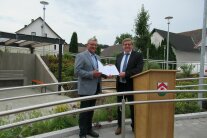 Zwei Herren stehen auf einem sanierten Gehweg in der Dorfmitte von Dornwang und halten eine Urkunde in ihren Händen.