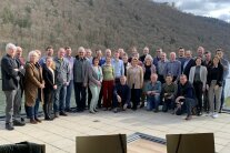 Insgesamt 36 Teilnehmerinnen und Teilnehmer am Gemeindeentwicklungs-Seminar posieren auf der Terrasse des Seminarhotels Wesenufer für ein Gruppenfoto am Flussufer der Donau. Auf der gegenüberliegenden Uferseite ist ein Hang mit Laubbäumen zu sehen.