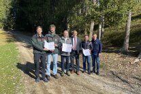 Sechs Herren stehen nebeneinander auf einem Waldweg am Kellerberg und halten Urkunden in ihren Händen.