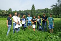 9 Personen stehen am Waldrand auf einer sommerlich blühenden Wiese. Zwei Damen tragen ein blaues Polo-Shirt mit dem Logo des ALE Niederbayern. Die sieben Jugendlichen halten verschiedene Präsente in ihren Händen.