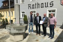 Vier Herren stehen neben dem Brunnen vorm Rathaus des Marktes Untergriesbach