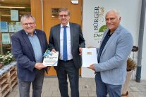 Drei Herren stehen vorm Eingang zum Dorfladen in Zeilarn und halten eine Plakette und eine Urkunde in ihren Händen