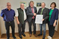 Vier Herren und eine Frau stehen nebeneinander im Gang vorm Bürgermeisterbüro des Marktes Windorf. Zwei Herren halten eine Urkunde in ihren Händen.