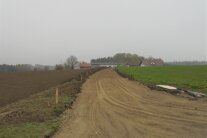 Der im Bau befindlicher Weg nach Quingl. Die Tragschicht für die spätere Asphaltdecke ist bereits aufgebracht. Im Hintergrund ist ein landwirtschaftliches Anwesen zu sehen.