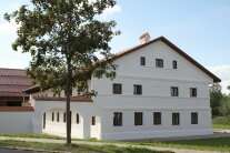 Außenansicht vom imposanten Wohnstallhaus des ehemaligen Wiesmerhofes. Links neben dem sanierten Gebäude befindet sich der Torbogen durch den man in den Innenhof des Anwesens gelangt. Im Hintergrund ist der Stadel zu sehen. Vor dem Gebäude, zur Straße hin, steht ein Laubbaum.