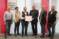 Zwei Damen und vier Herren stehen vor rot-beigen Streifen-Vorhängen auf denen das Gemeindewappen zu sehen ist. 