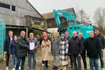 Neune Herren und vier Damen stehen nebeneinander vor dem leerstehenden Gutshof in Innernzell. Hinter ihnen befindet sich ein Bagger.