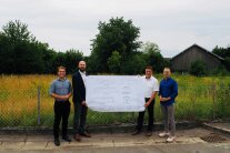 Vier Herren stehen auf dem Baugrund für das neue Oberschneidinger Schulhaus und halten einen Bauplan in ihren Händen.