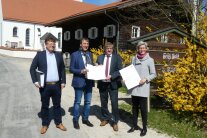 Drei Herren und eine Dame stehen vorm Ortseingang von Waldhof und halten eine Urkunde in ihren Händen.