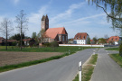 Eine Straße mit einem Radweg führt auf das Dorf Oberdietfurt zu. Im Hintergrund erkennt man die Kirche aus Backsteinen und das mächtige verputzte Pfarrhaus rechts daneben.