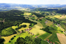 Auf dem sonnigen Luftbild der hügeligen Landschaft des bayerischen Waldes bei Gottlesried, Lkr. Regen, ist die Einteilung der Felder, Wiesen und der üppigen Bewaldung zu sehen.