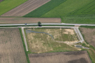Luftbild eines neu angelegten Wasserrückhaltebeckens neben Feldern und einer Landstraße, die nach Mitterndorf, Lkr. Deggendorf, führt.