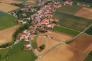 Vogelperspektivaufnahme: Das lang gestreckte Dorf Schambach und die in durchschnittlich 150 Metern Entfernung vorbeiführende Umgehungsstraße mit zwei Abzweigen zum Dorf.