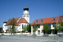 Ein gepflasterter Platz mit mehreren in die Fläche eingebundenen Bäumen, daneben die imposante Kirche.